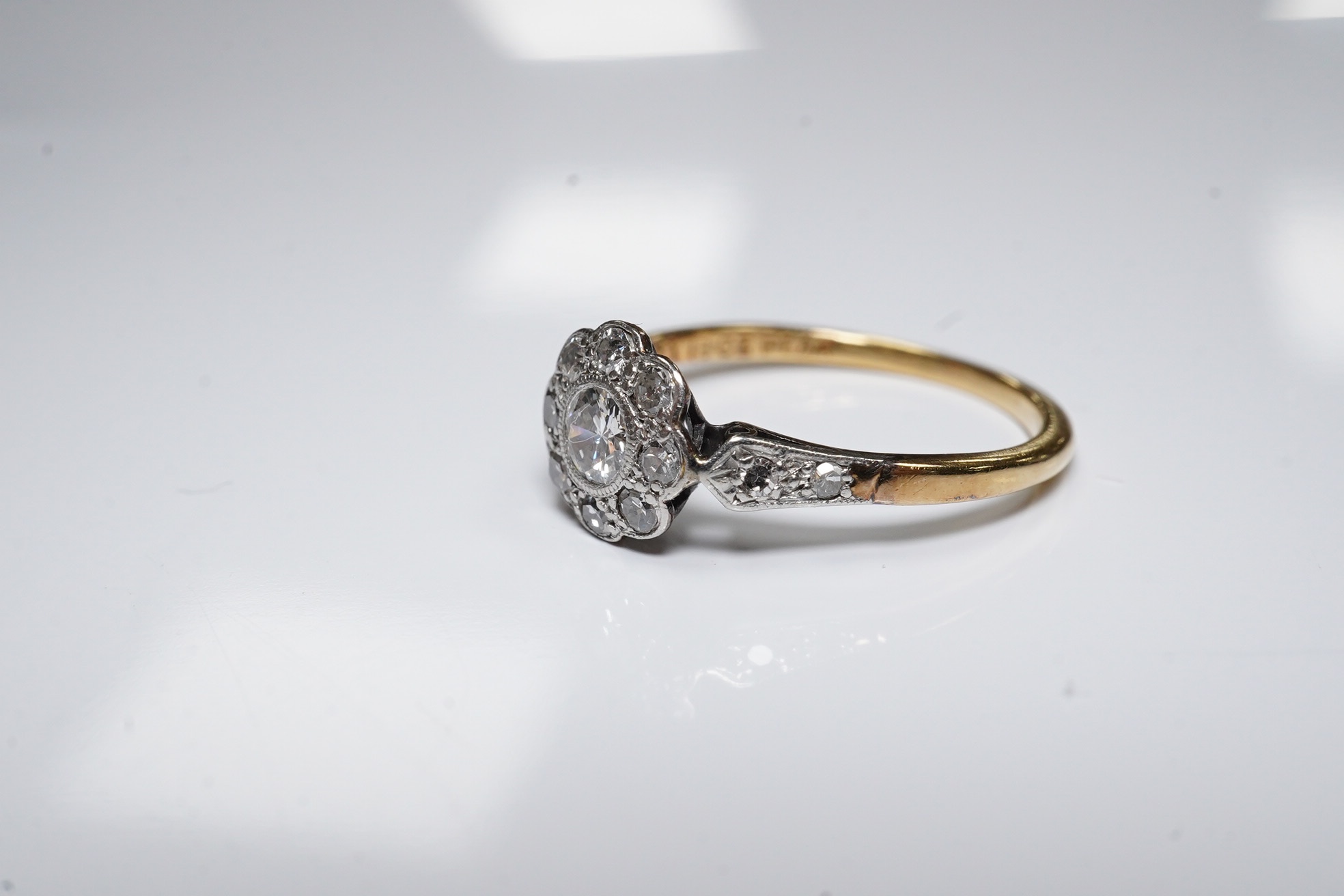 A 1920's 18ct, plat and millegrain set diamond cluster ring, with diamond set shoulders, size N, gross weight 2.4 grams. Condition - fair